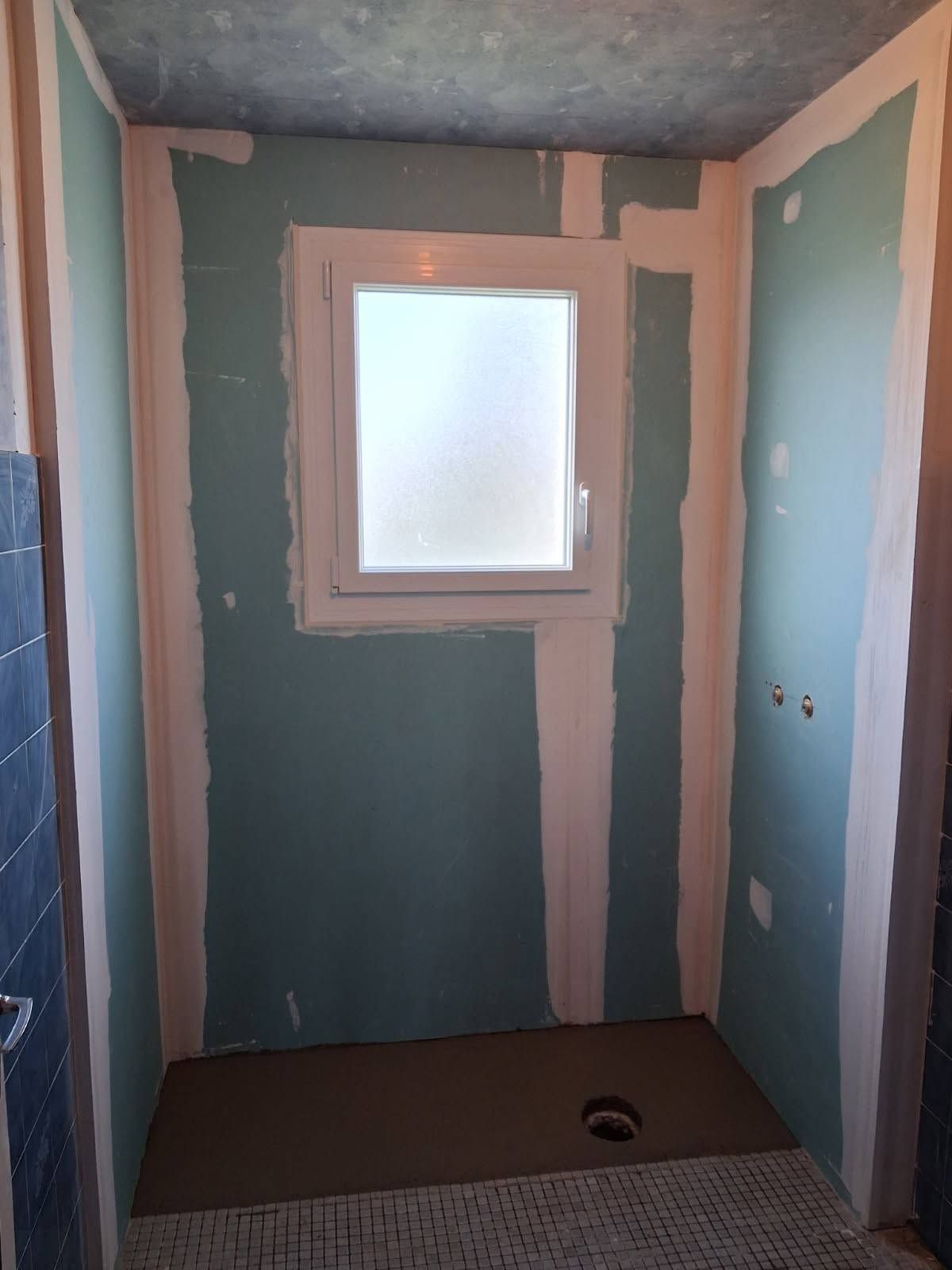 Pièce inachevée avec murs blancs, échelle, établi et grande fenêtre en cours de rénovation
