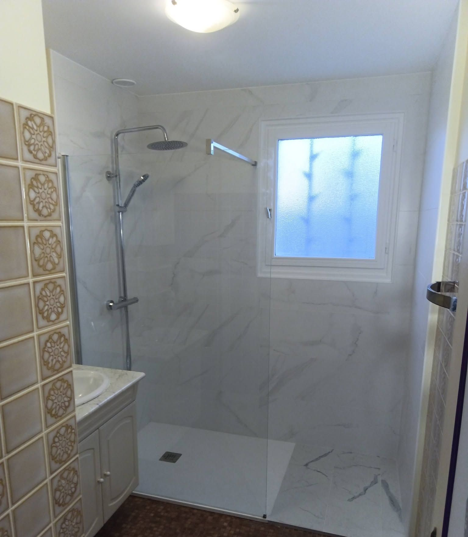 Salle de bains avec douche en marbre blanc, fenêtre dépolie et meuble-lavabo.