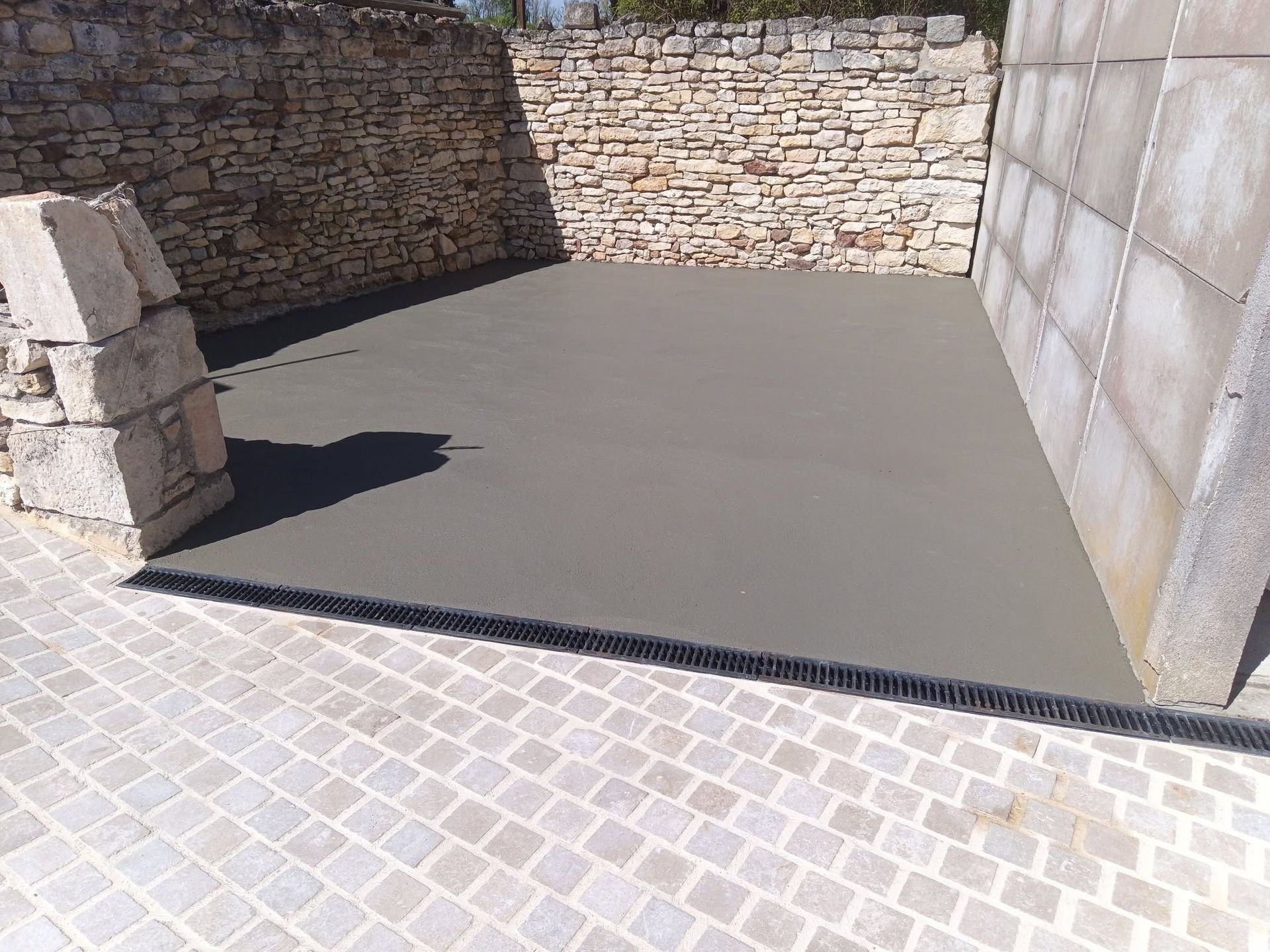 Cour pavée avec murs en pierre, dalle de béton et allée carrelée ensoleillée