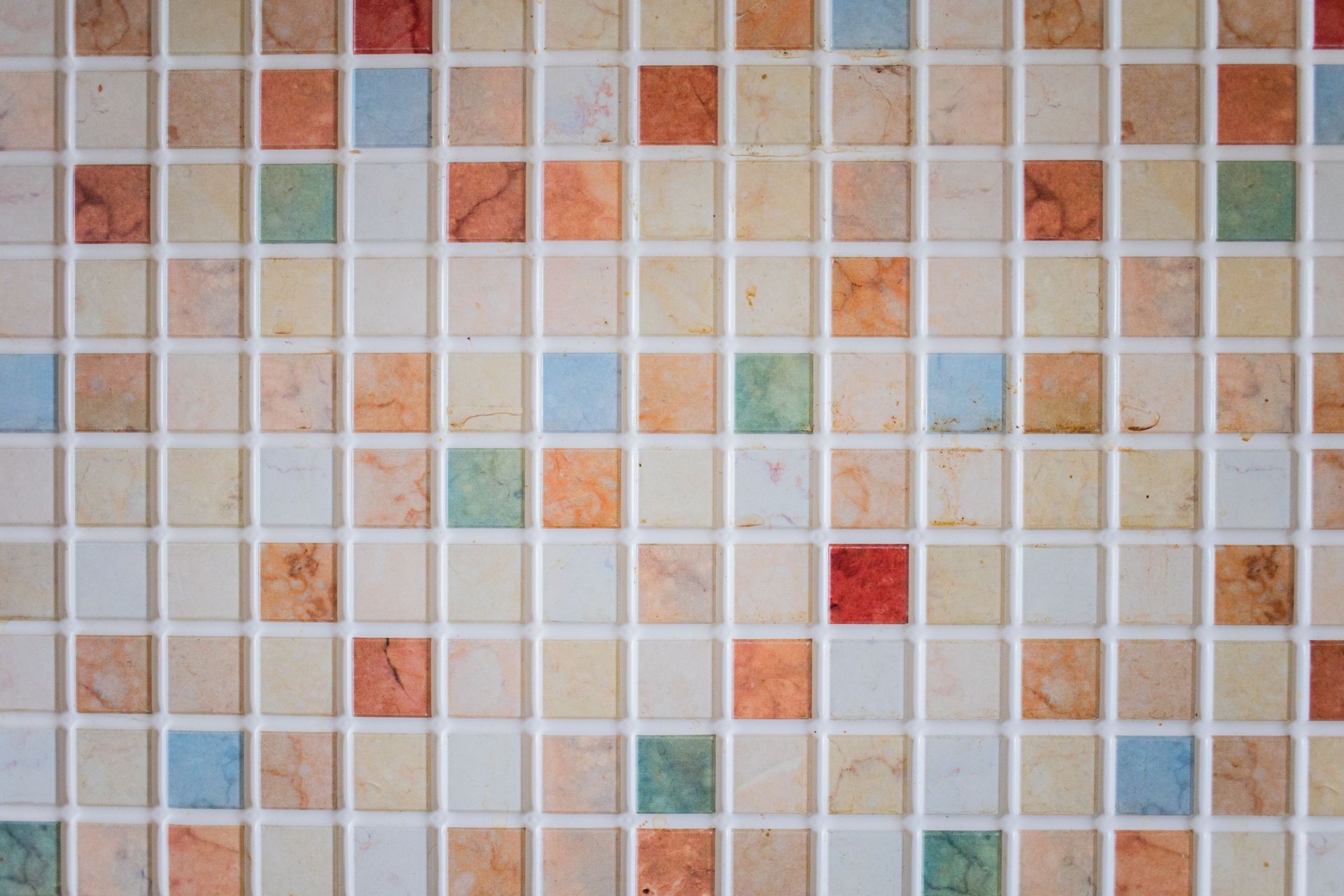Mur en mosaïque de petits carreaux beiges, bruns et pastel avec quelques touches de rouge et de vert