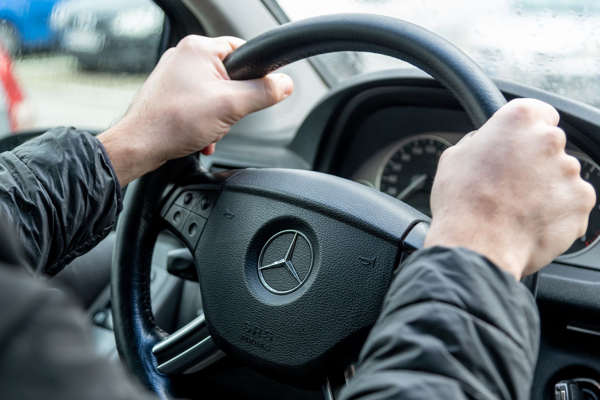 Hände, die während der Fahrt auf einer Strasse das Lenkrad eines Mercedes umklammern.