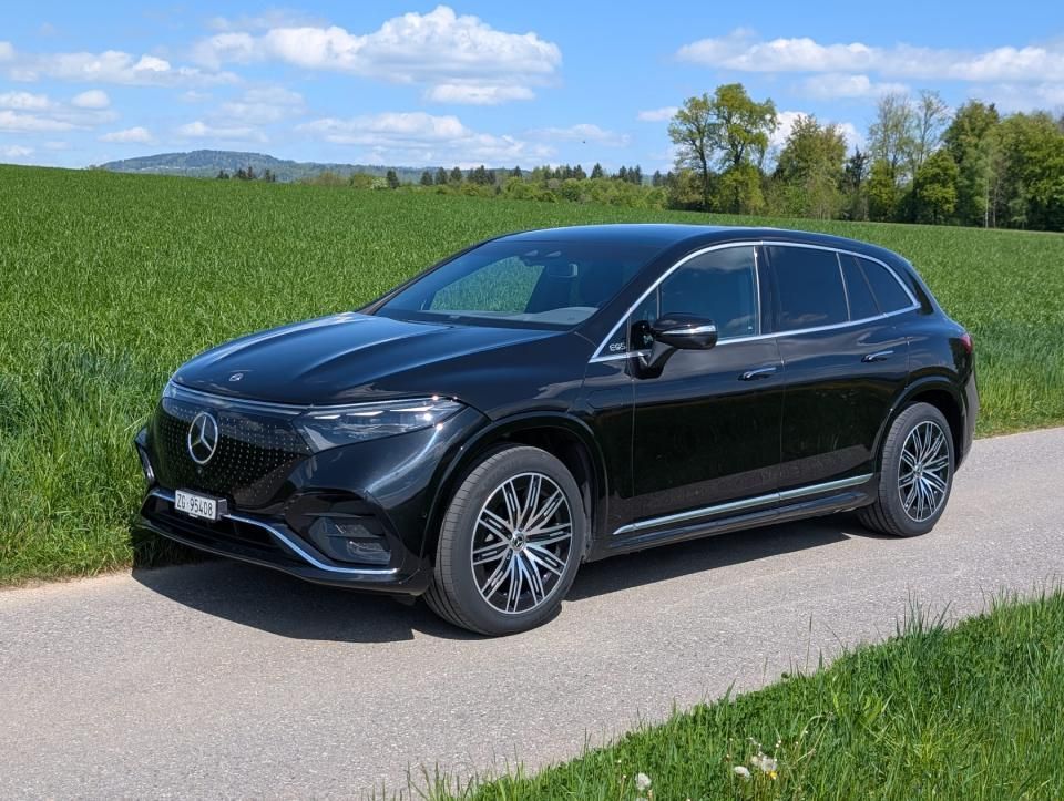 Ein schwarzer Lieferwagen parkt auf einer Landstrasse neben grünen Feldern unter blauem Himmel