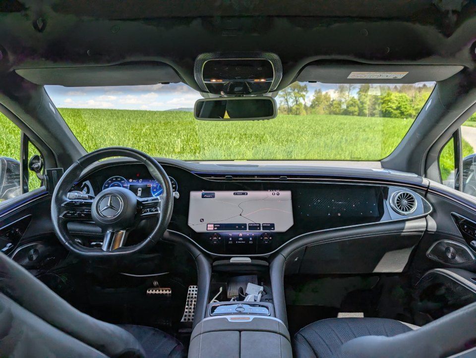Moderner Fahrzeuginnenraum mit schwarzem Armaturenbrett, Lenkrad und zentralem Touchscreen, von der Rückbank aus gesehen.