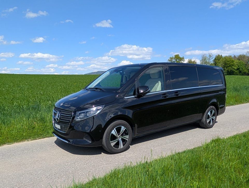 Ein schwarzer Lieferwagen parkt auf einer Landstrasse neben grünen Feldern unter blauem Himmel