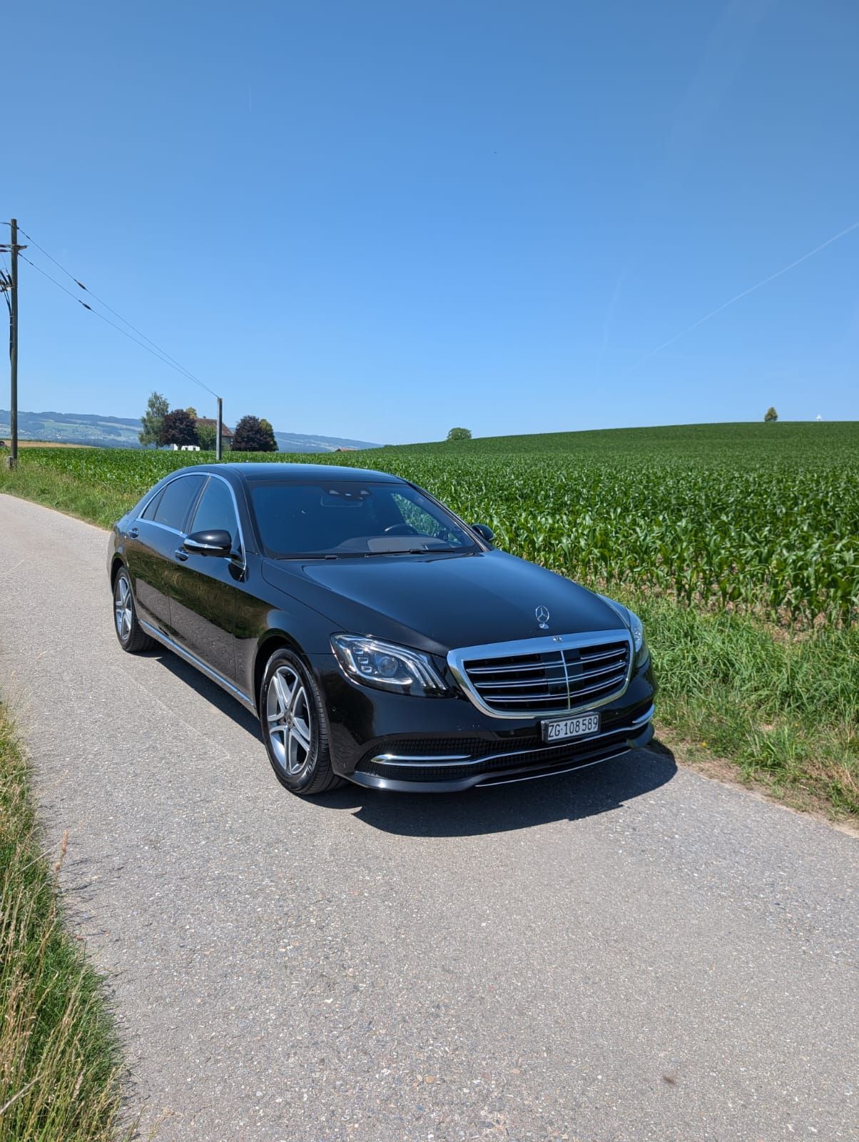 Ein schwarzer Mercedes-Transporter parkt auf einer Landstrasse neben einem grünen Feld unter blauem Himmel.