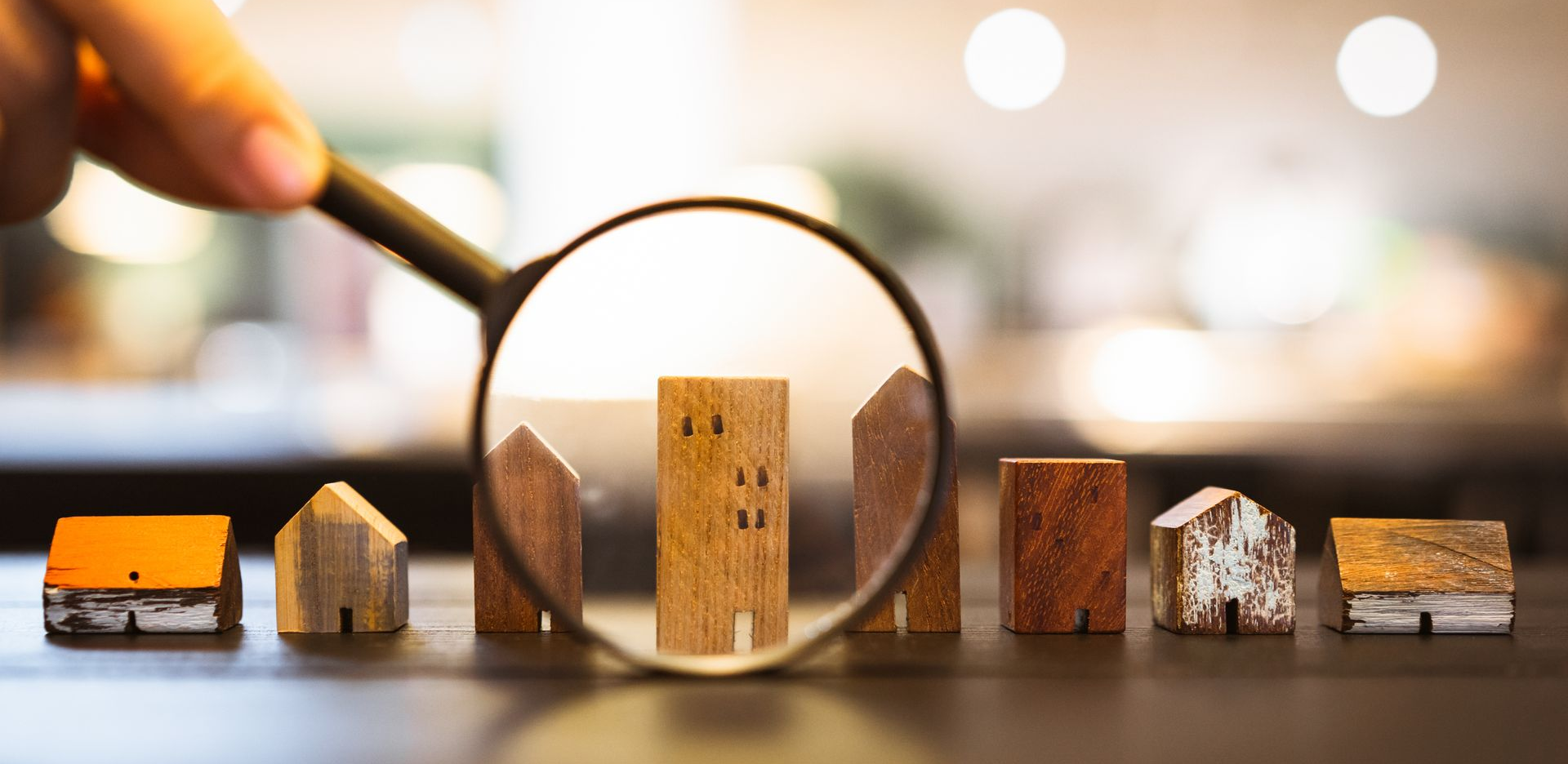 Main tenant une loupe au-dessus de maisons miniatures.