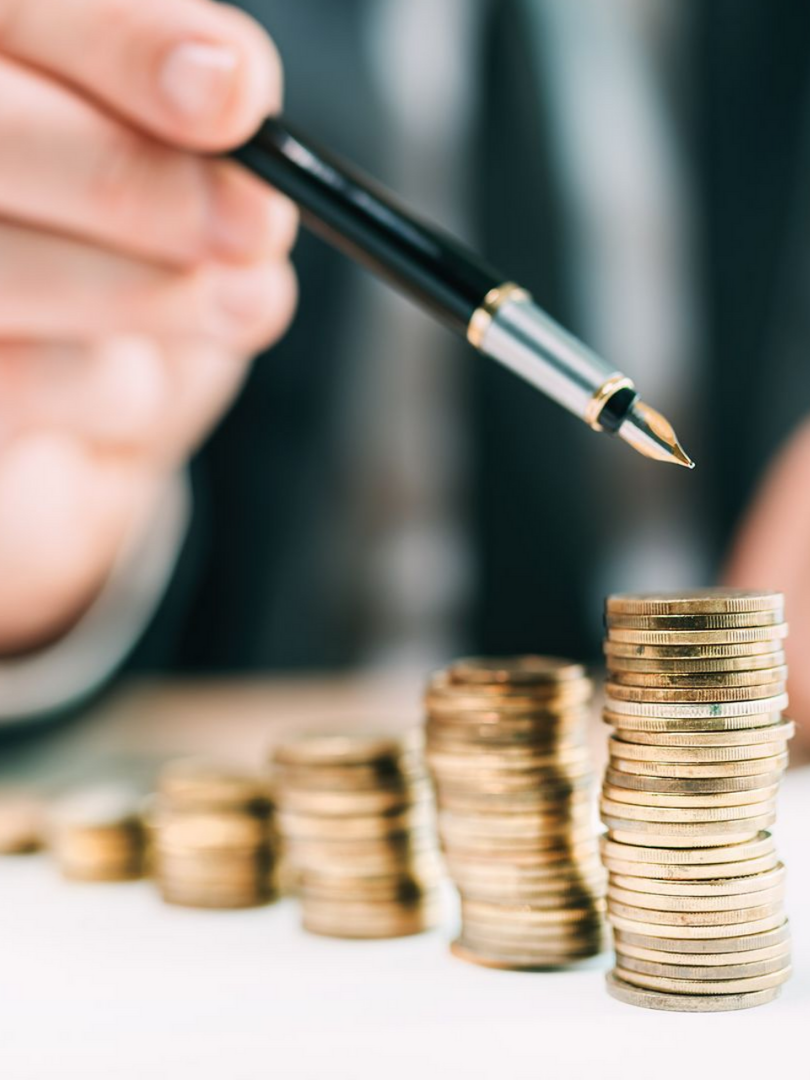Un stylo désigne des piles de pièces de monnaie, illustrant la croissance financière.