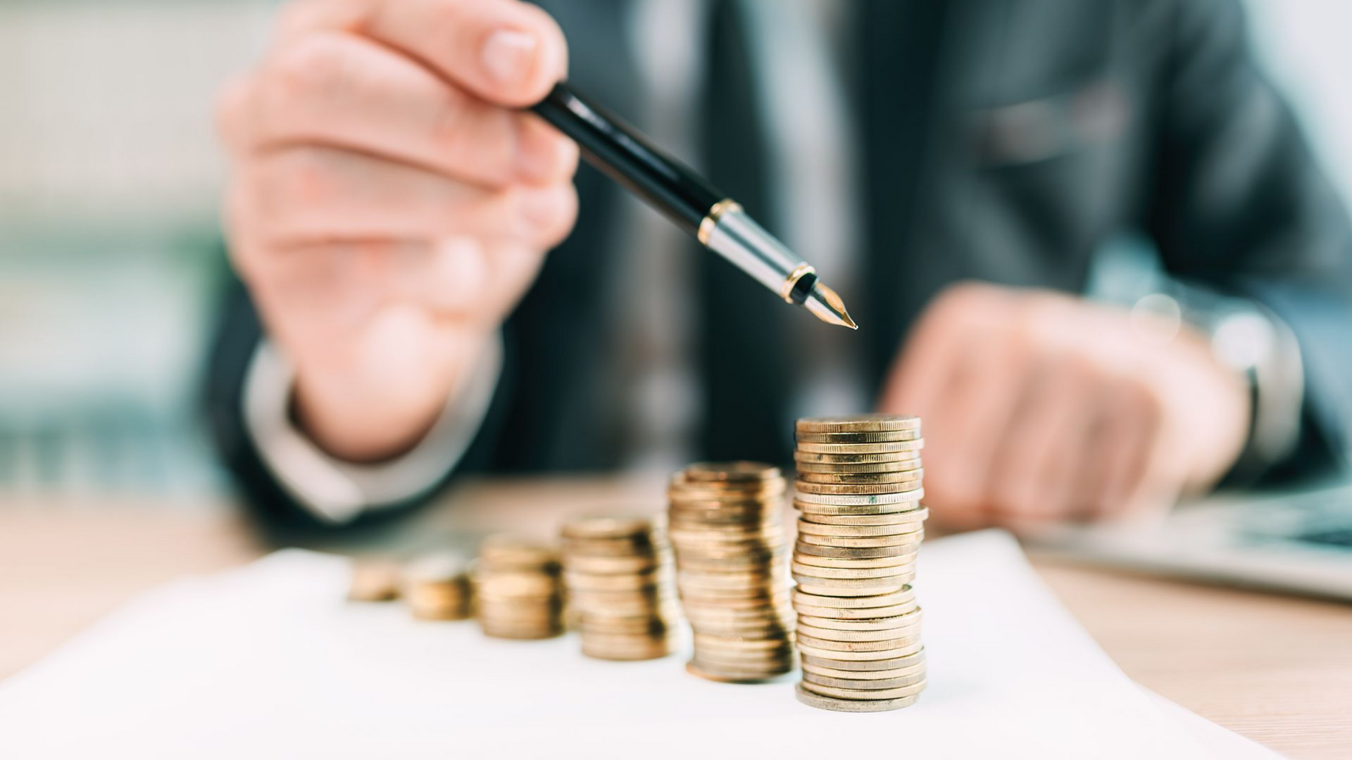 Un homme en costume pointe un stylo vers des piles de pièces qui s'accumule, symbolisant la croissance financière.
