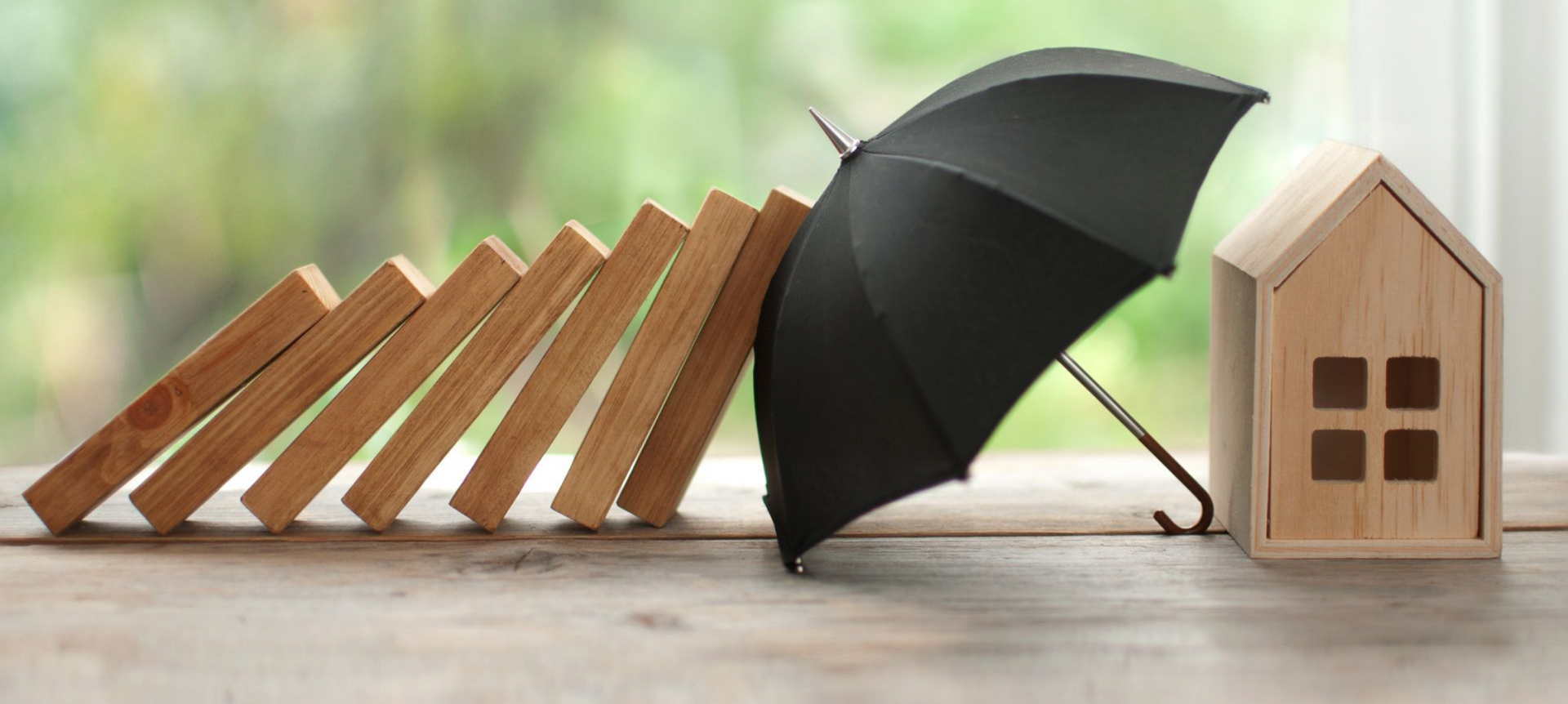 Un parapluie protège une maison miniature des dominos qui tombent.