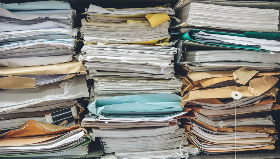Des piles de documents de bureau, de dossiers et de papiers empilés en désordre sur des étagères.