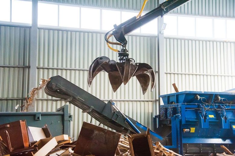 Une pince mécanique suspendue au-dessus d'un tapis roulant dans une installation de traitement des déchets industriels.