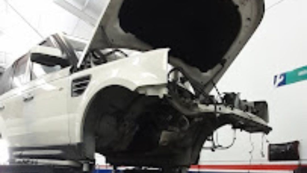 Un coche blanco está siendo reparado en un garaje con el capó abierto.