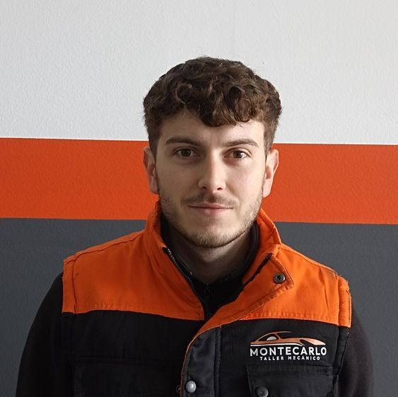 Un hombre que lleva un chaleco negro y naranja está parado frente a una pared.