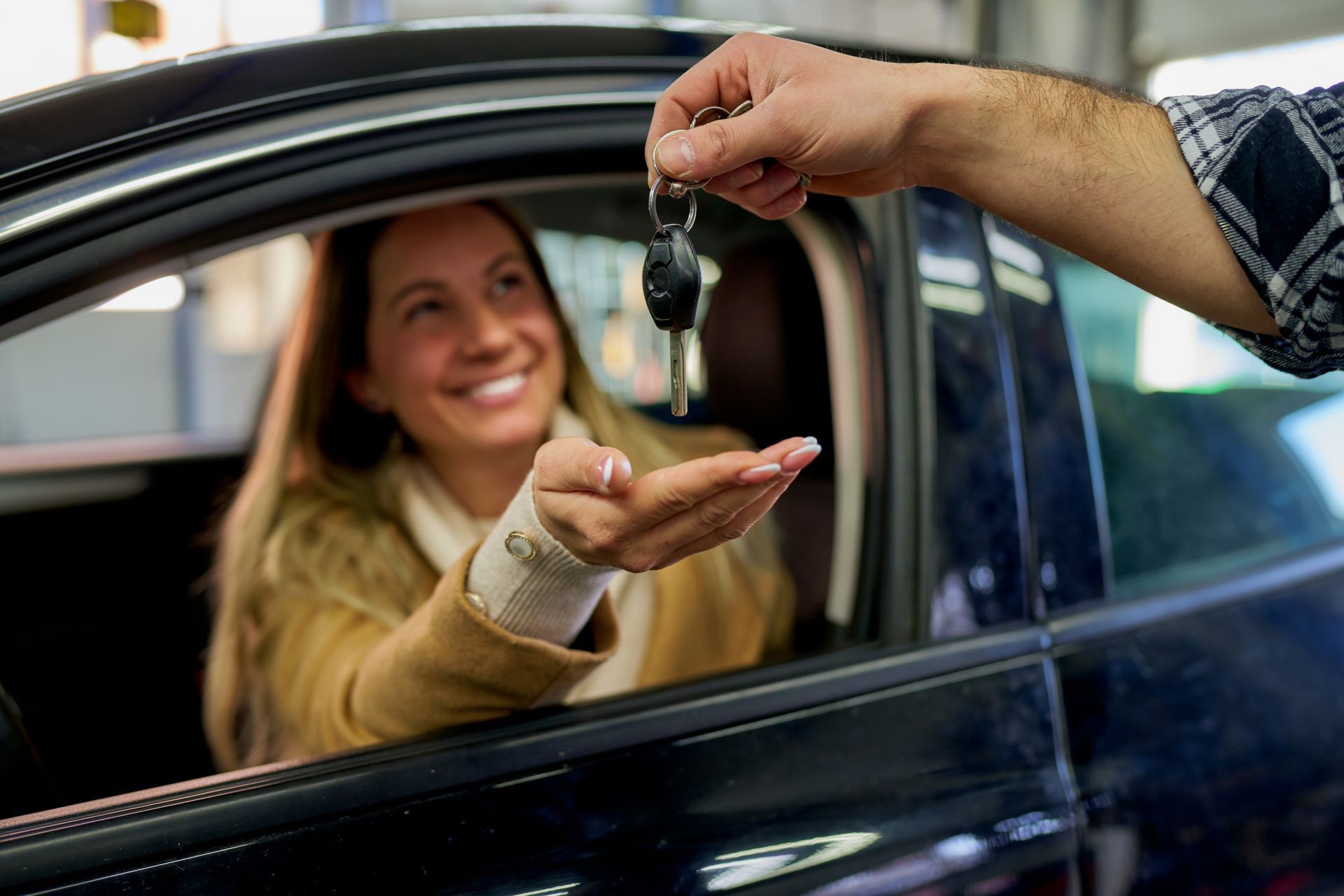 Une personne dans une voiture reçoit les clés d'une autre personne ; sourire, garage.