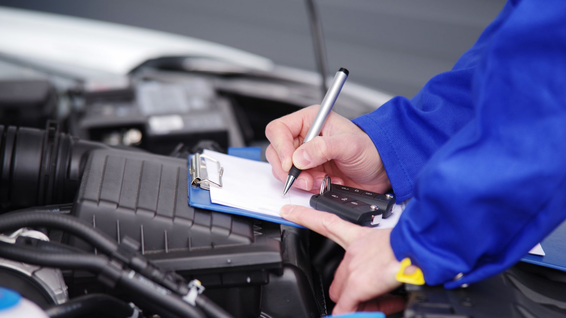 Un mécanicien en combinaison bleue prend des notes sur un bloc-notes tout en inspectant un moteur de voiture.
