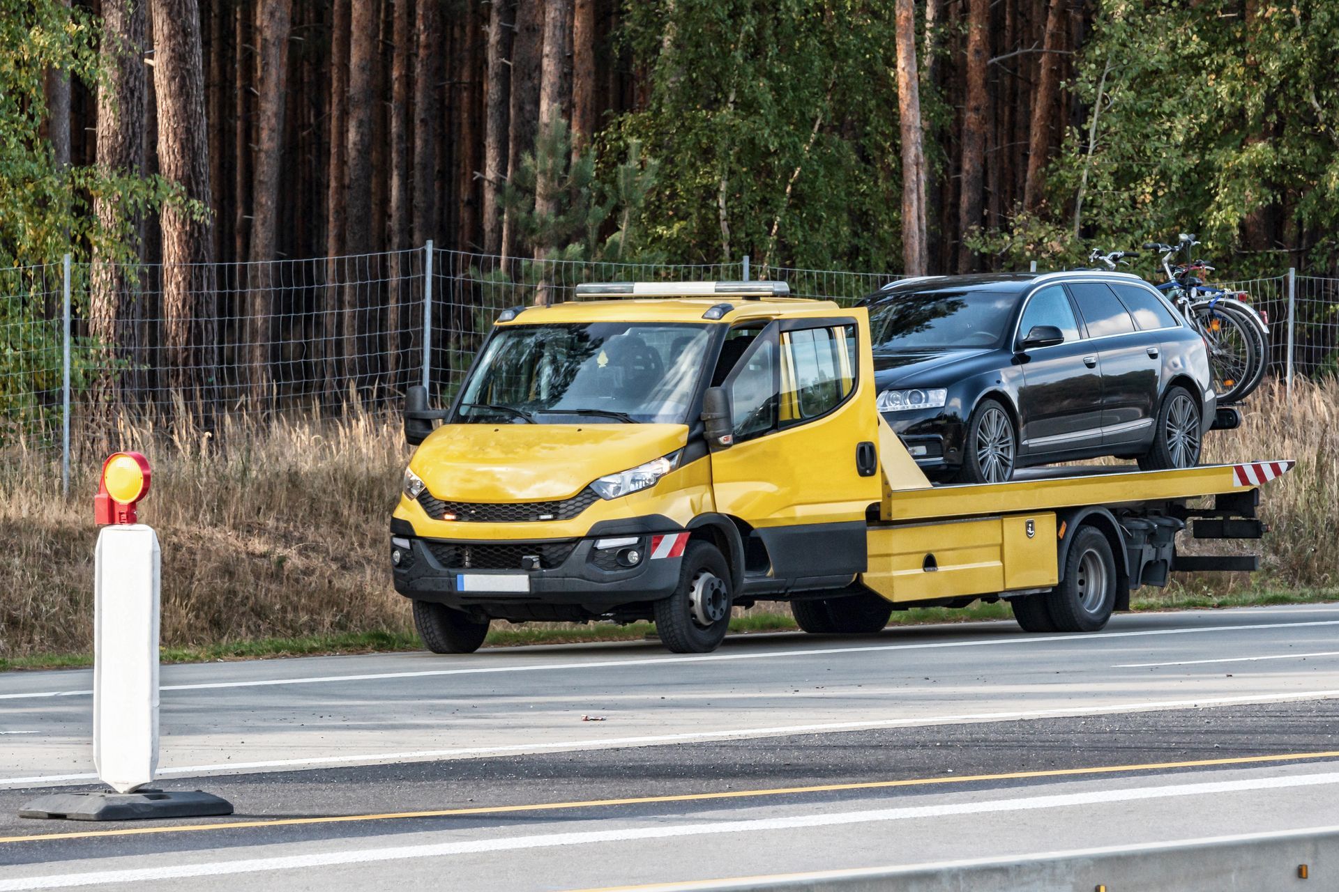 Une dépanneuse jaune transporte une voiture noire sur une autoroute, avec des arbres en arrière-plan.