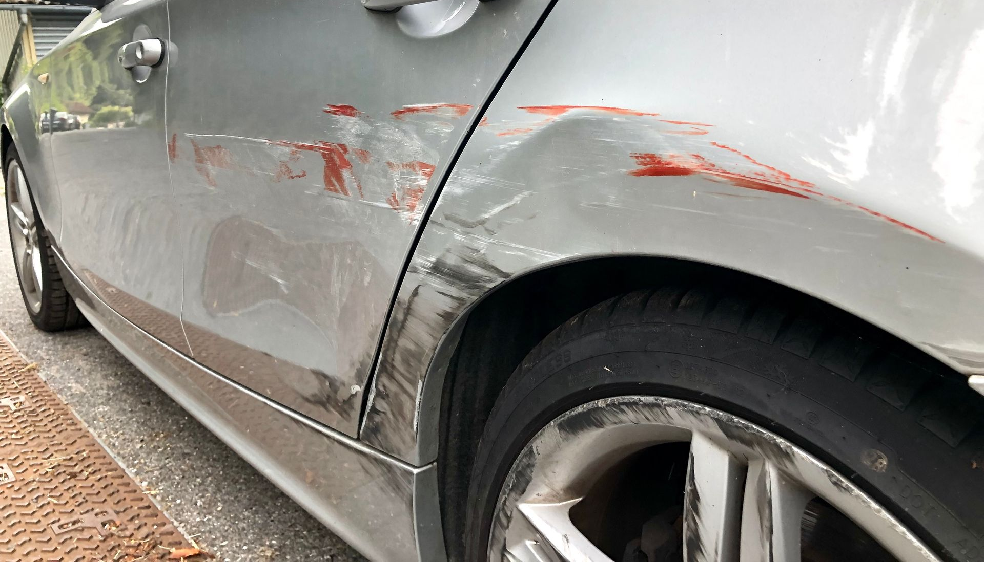 Voiture argentée endommagée, panneau arrière cabossé avec des rayures et des marques rouges.