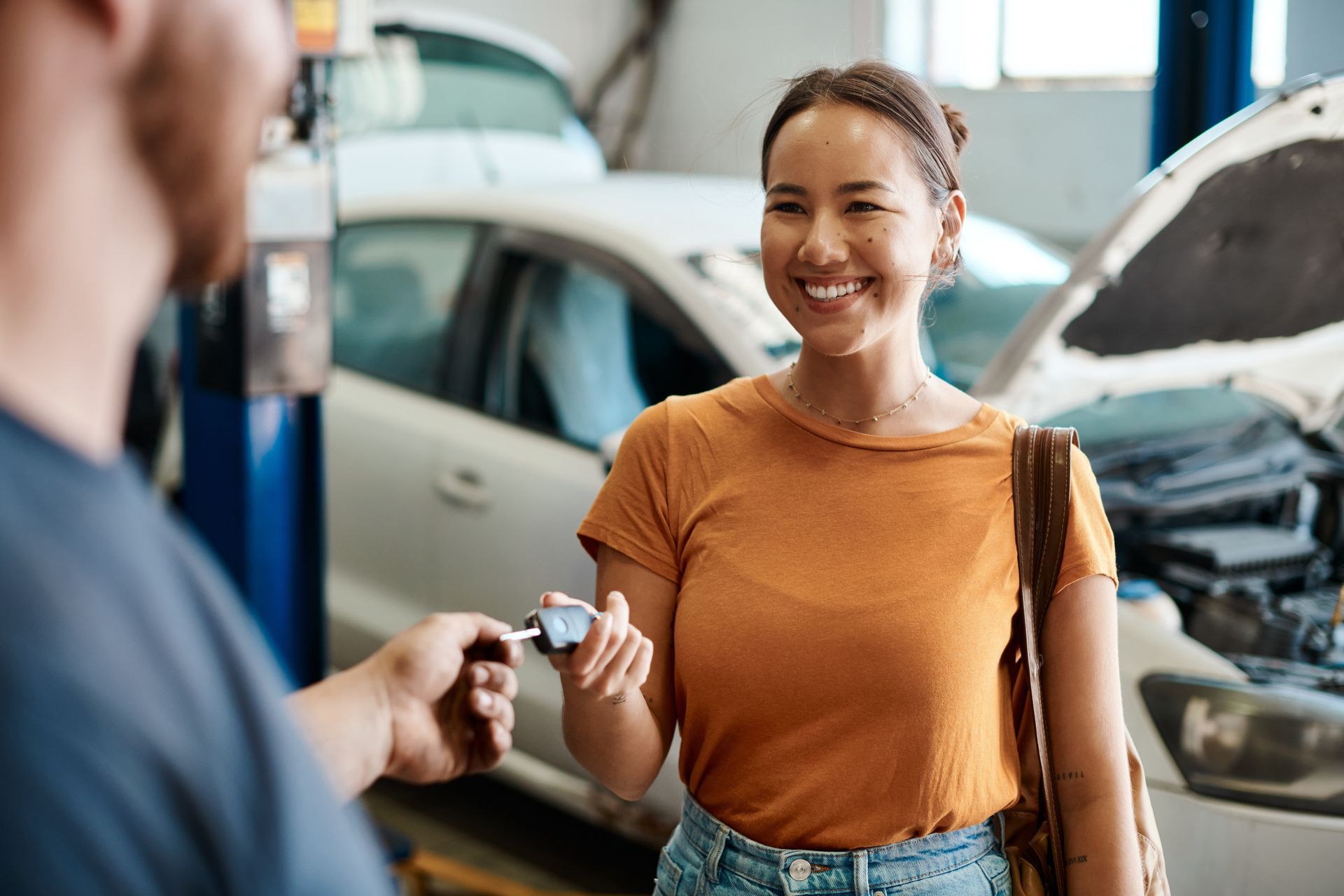 Femme souriante recevant les clés de sa voiture d'un mécanicien dans un garage ; capot ouvert en arrière-plan.