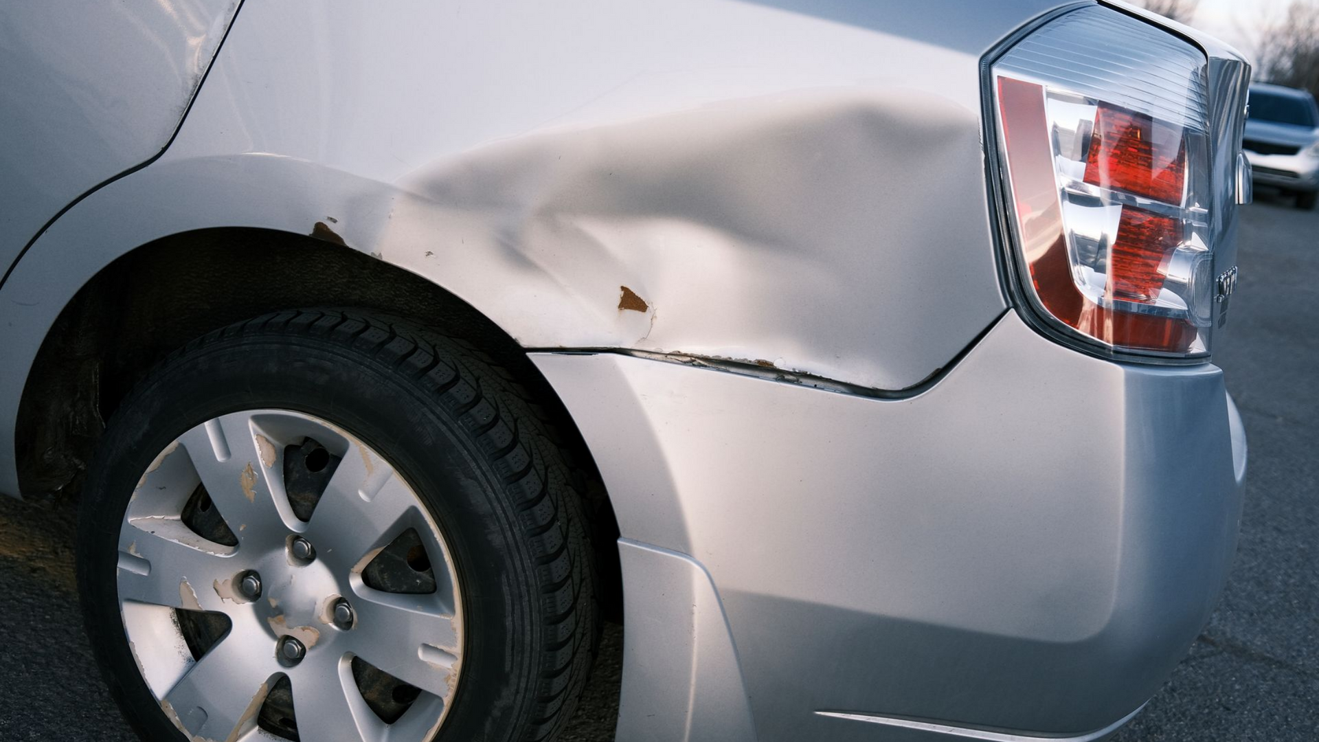 Voiture argentée avec un important enfoncement sur l'aile arrière et des traces de rouille.