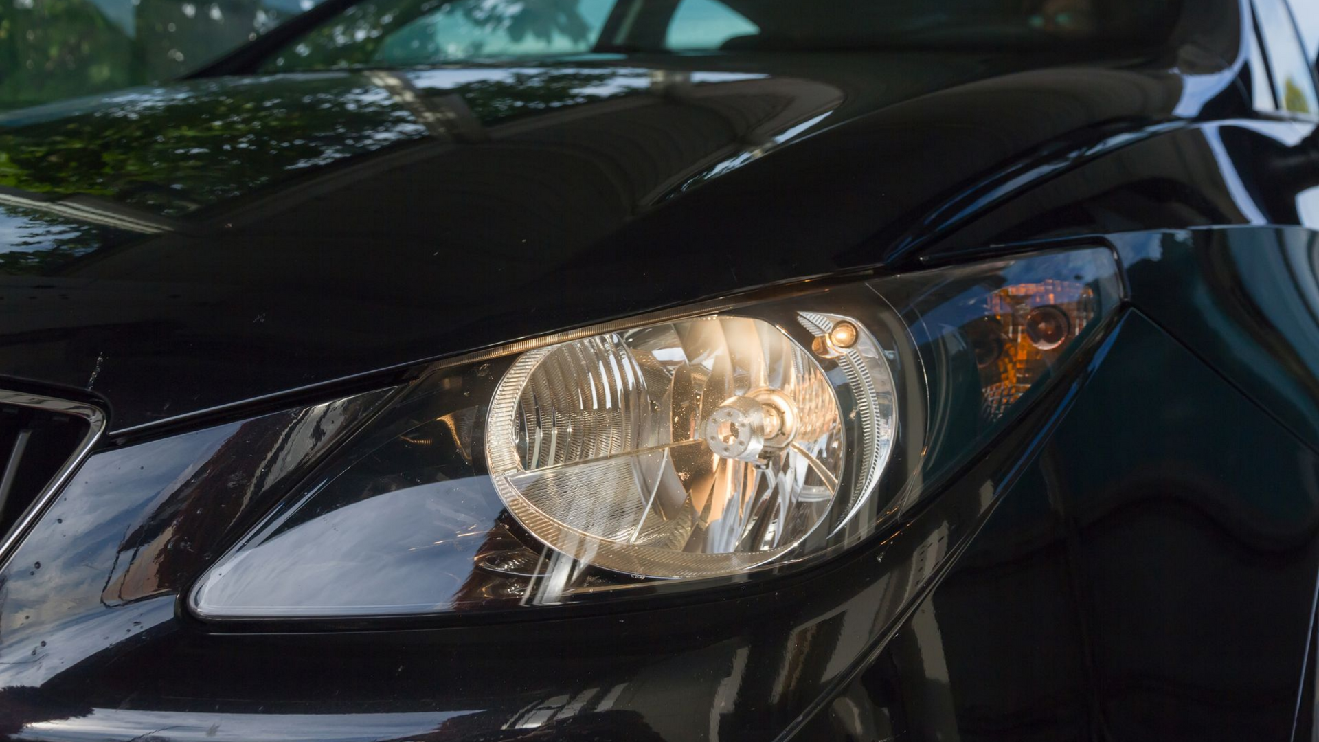 Gros plan sur le phare d'une voiture noire ; ampoule allumée, surface noire brillante.