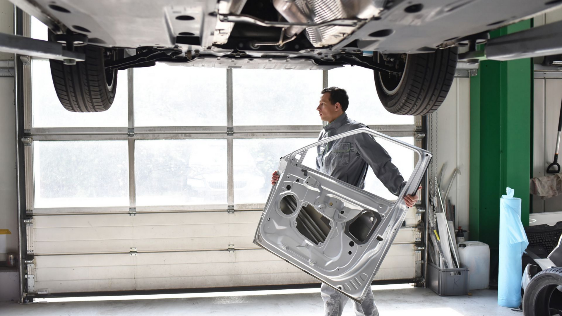 Un mécanicien tient la portière d'une voiture sous celle-ci, soulevée par un pont élévateur dans un garage.