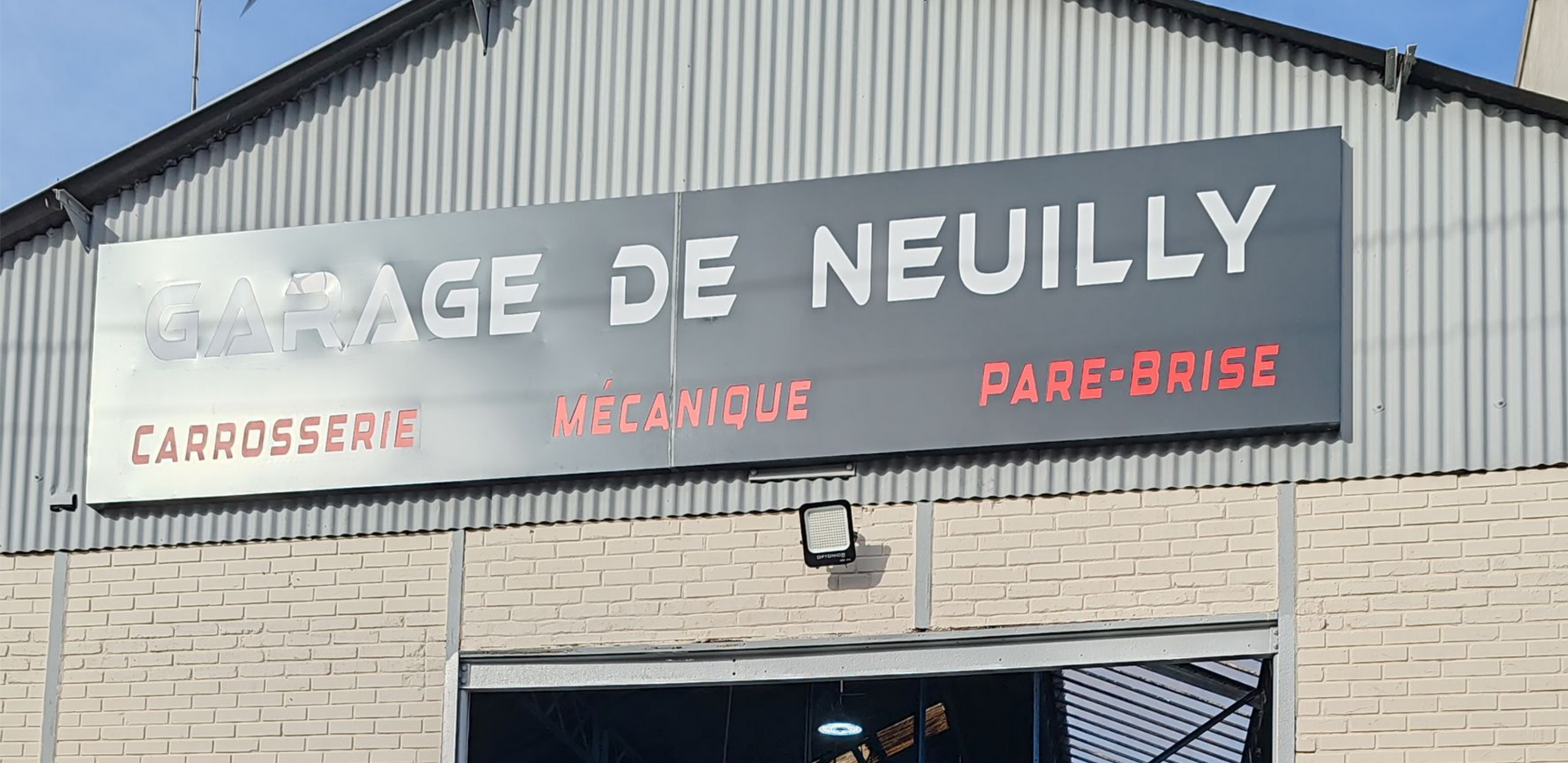 Panneau de garage GARAGE DE NEUILLY, avec les services listés en rouge. Vue extérieure.