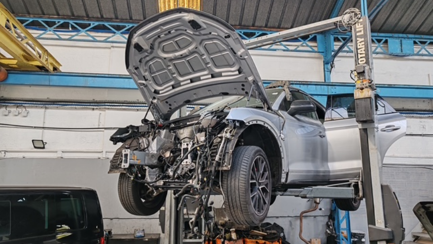 Voiture argentée soulevée sur un pont élévateur dans un atelier de réparation, capot ouvert et avant endommagé.