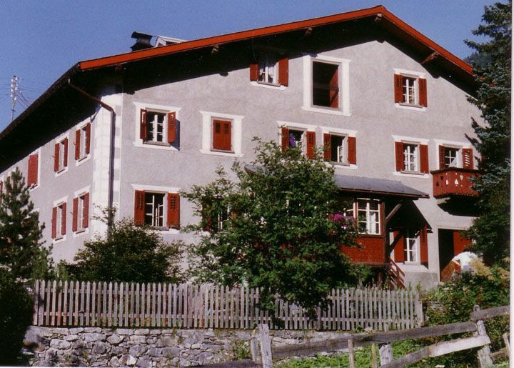Ein grosses Haus mti roten Fensterläden, im Vordergrund ein alter hölzerner Gartenzaun