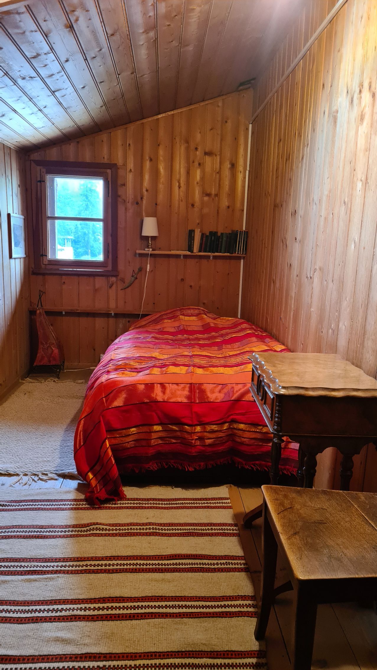Ein schmales Schlafzimmer mit einem roten Bettüberwurf auf dem Bett und getäferten Wänden.