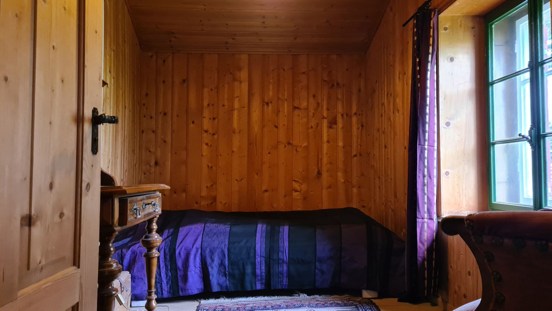 Ein Schlafzimmer mit Täferwänden und einem violetten Überwurf auf dem Bett.