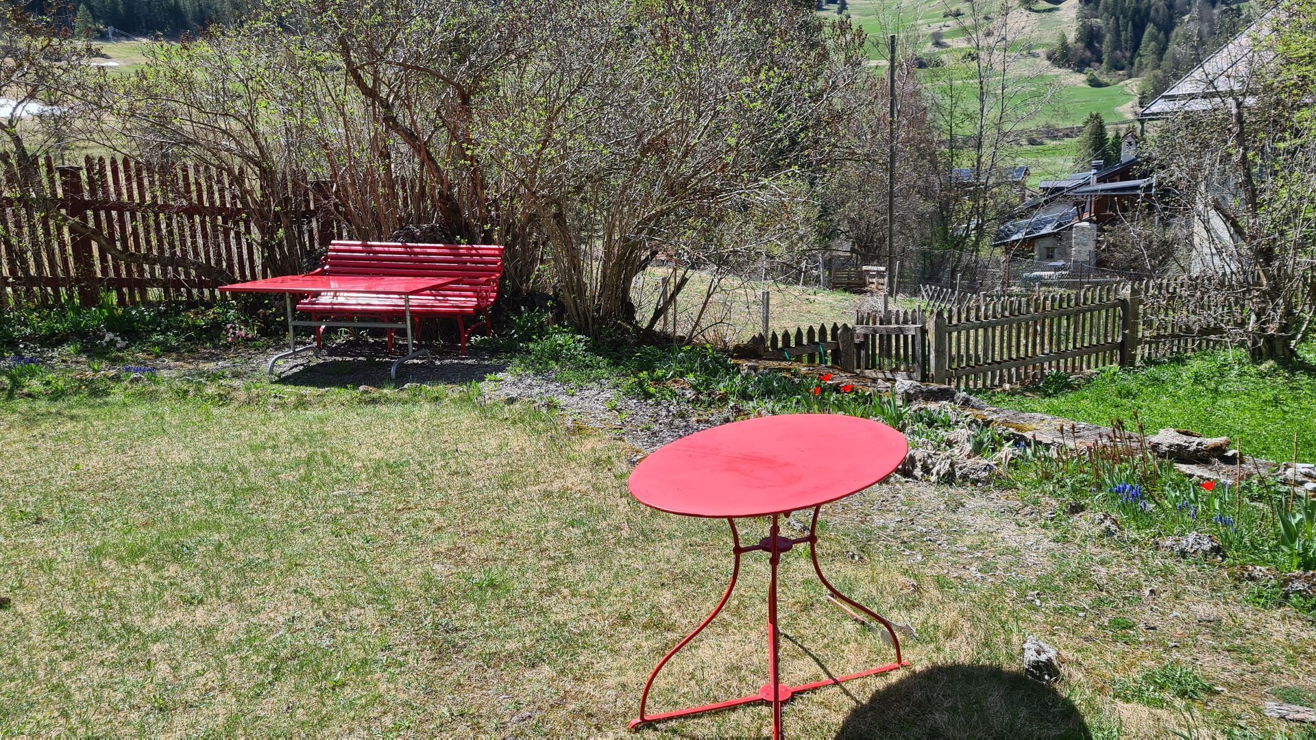 Ein antiker Gartentisch aus rotem Metall steht auf einer noch kahlen Wiese.
