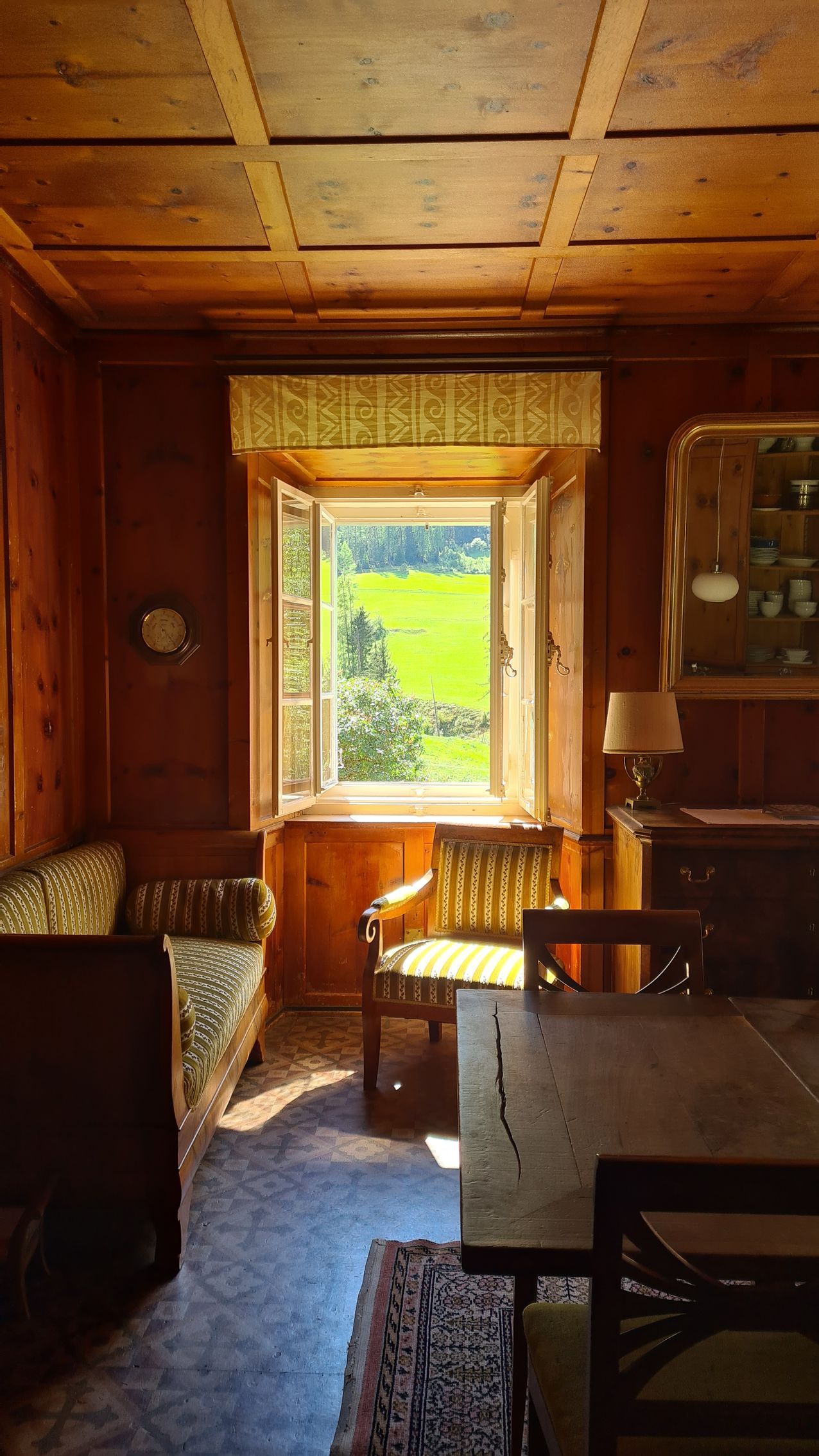 Ausblick aus einem Fenster ins Grüne, innen antike Möbel und braunes Wandtäfer