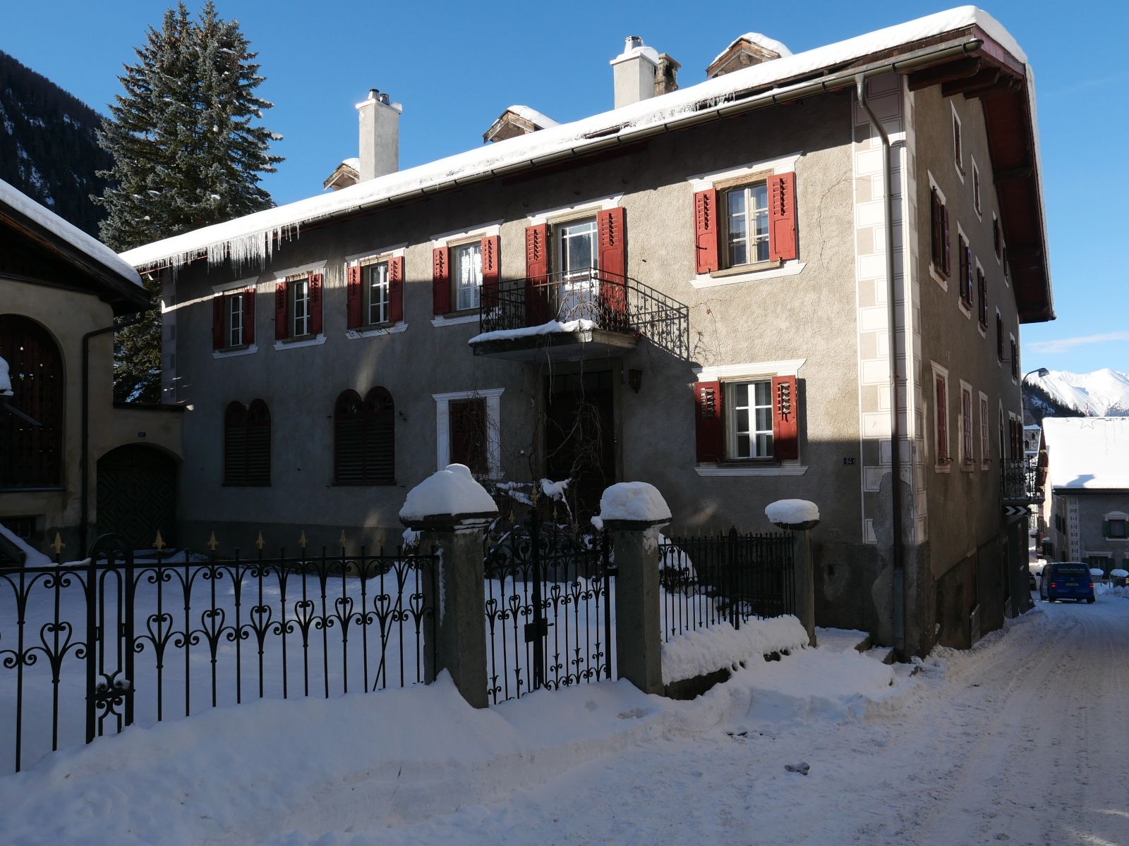 Ein grosses Haus mit roten Fensterläden, davor ein Schmiedeisenzaun, mit viel Schnee.