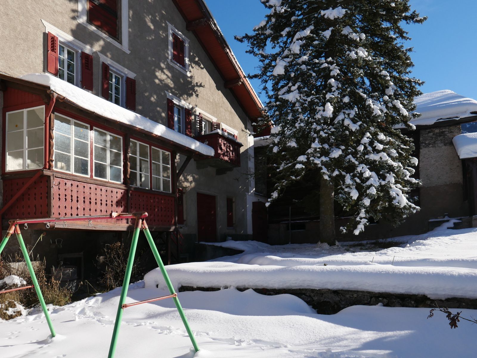 Ein grosses Haus mit roten Fensterläden und einer roten Holzveranda, davor ein schneebedeckter Garten