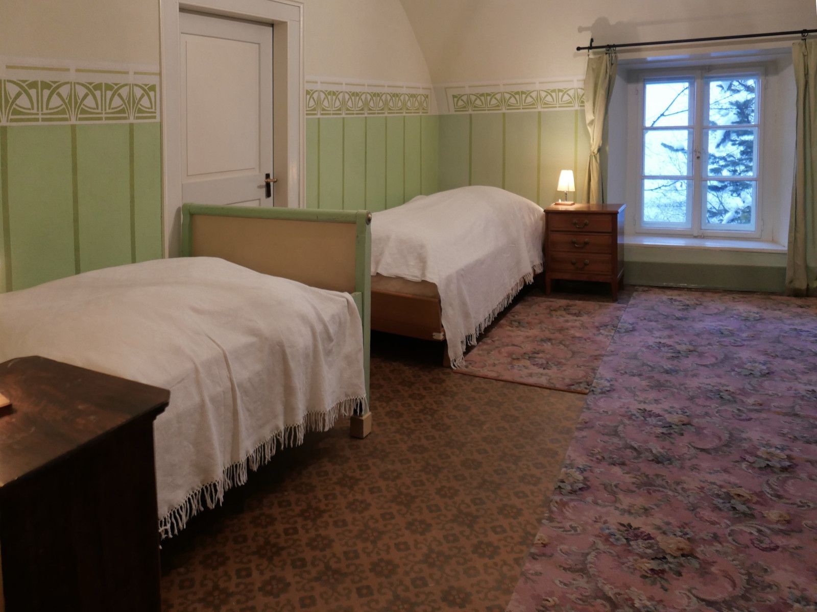 Ein Schlafzimmer mit grünen Jugendstilmalereien an den Wänden und zwei Einzelbetten