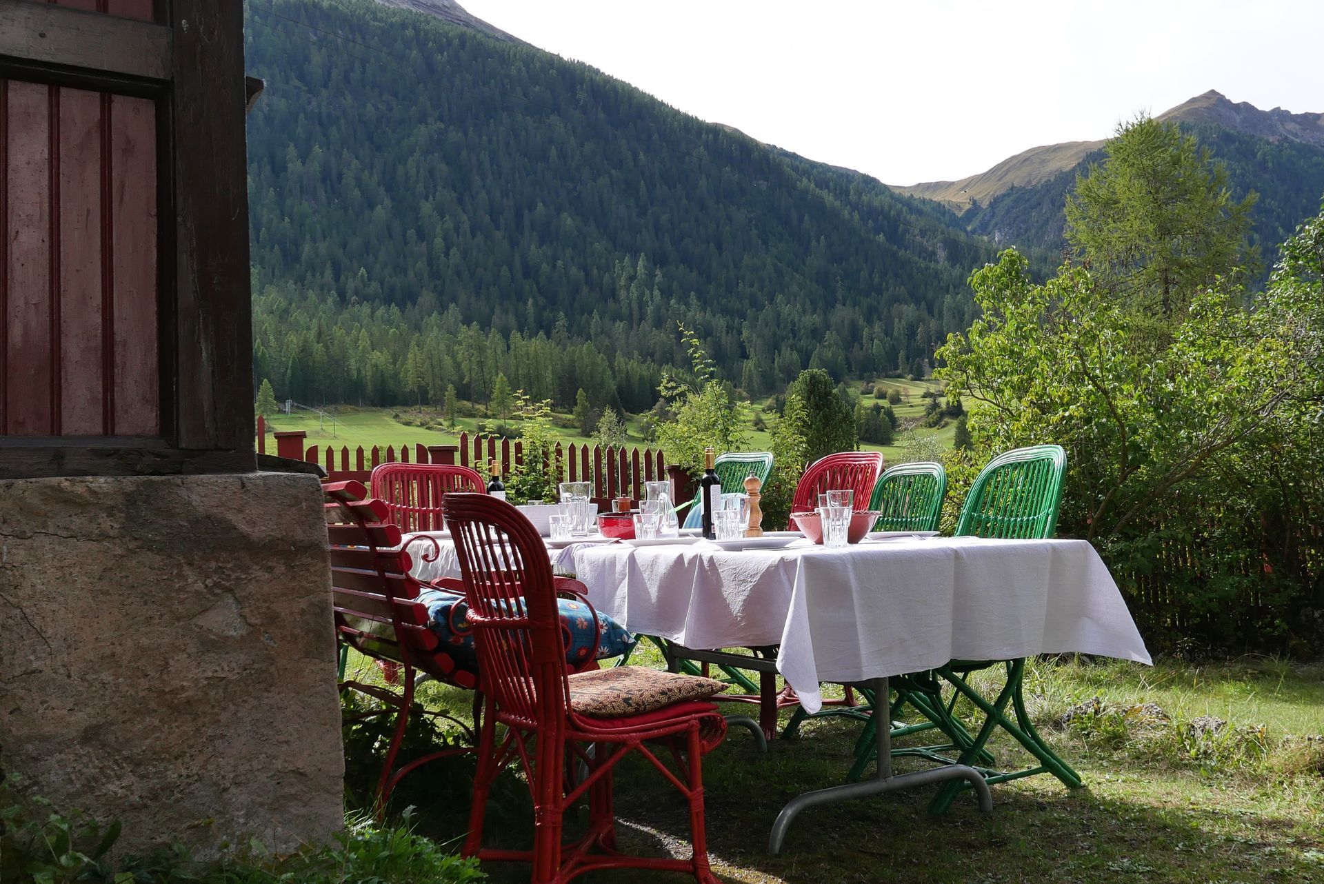 Ein langer gedeckter Tisch mit Korbstühlen in einem Garten bei Sonnenschein
