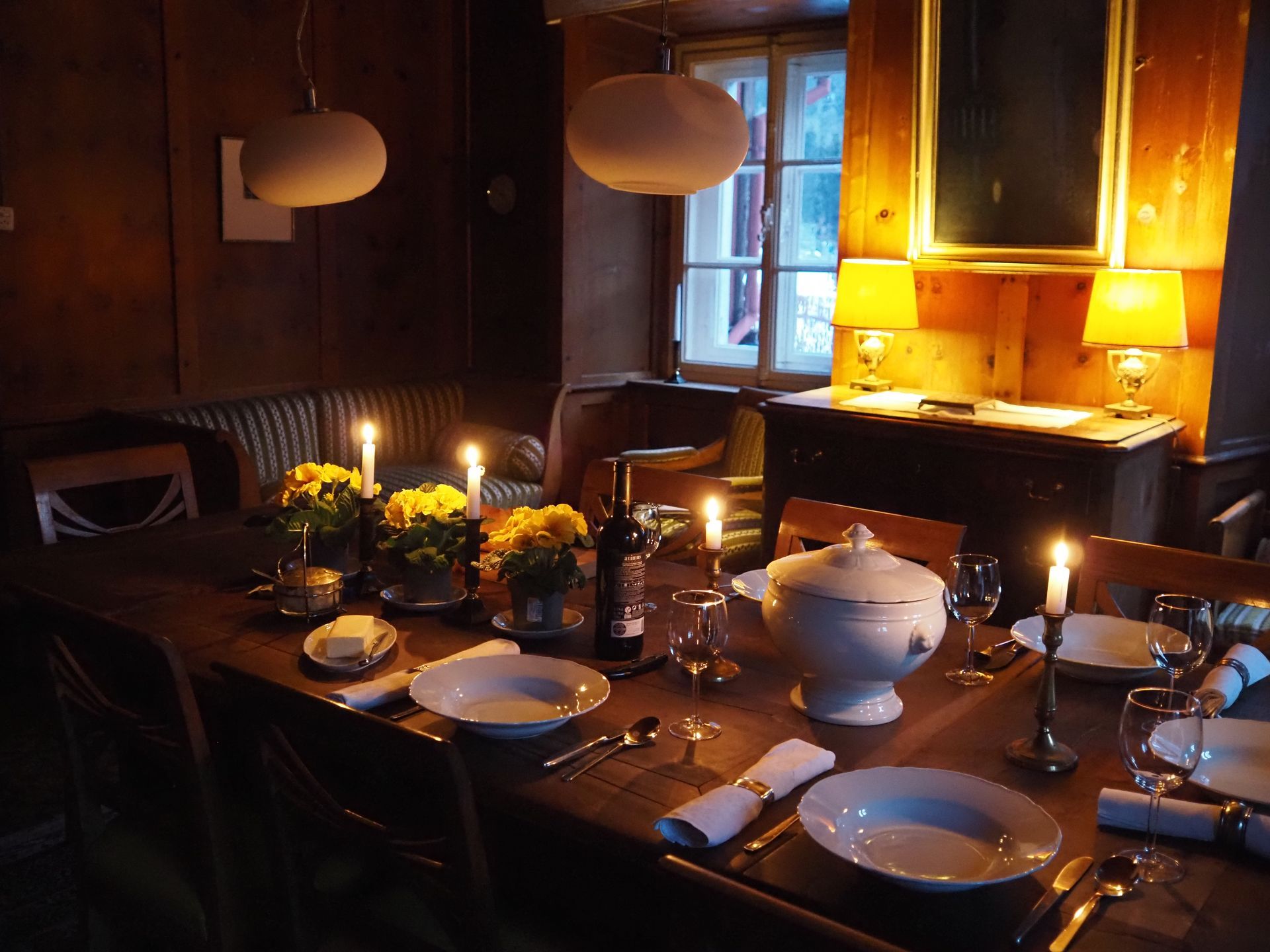 Ein festlich gedeckter Tisch mit Blumen und Kerzen, im Hintergrund zwei Tischlampen mit Stoffschirmen und Messingsockeln.