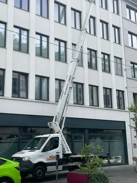 Ein weißer LKW mit ausgefahrener Hebebühne steht neben einem mehrstöckigen Gebäude.