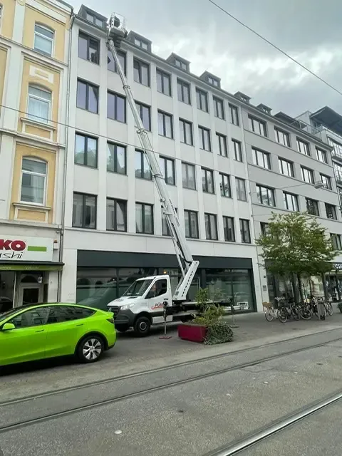 Ein weißer Lastwagen mit einer Hebebühne, die zu einem mehrstöckigen Gebäude in einer Stadtstraße führt.