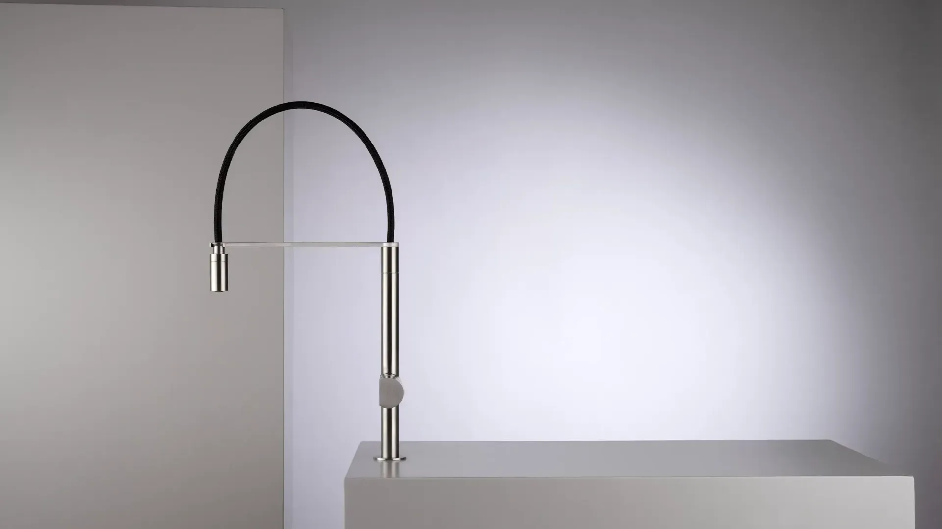 Grifo plateado con caño negro curvo sobre una superficie blanca contra una pared con degradado blanco.