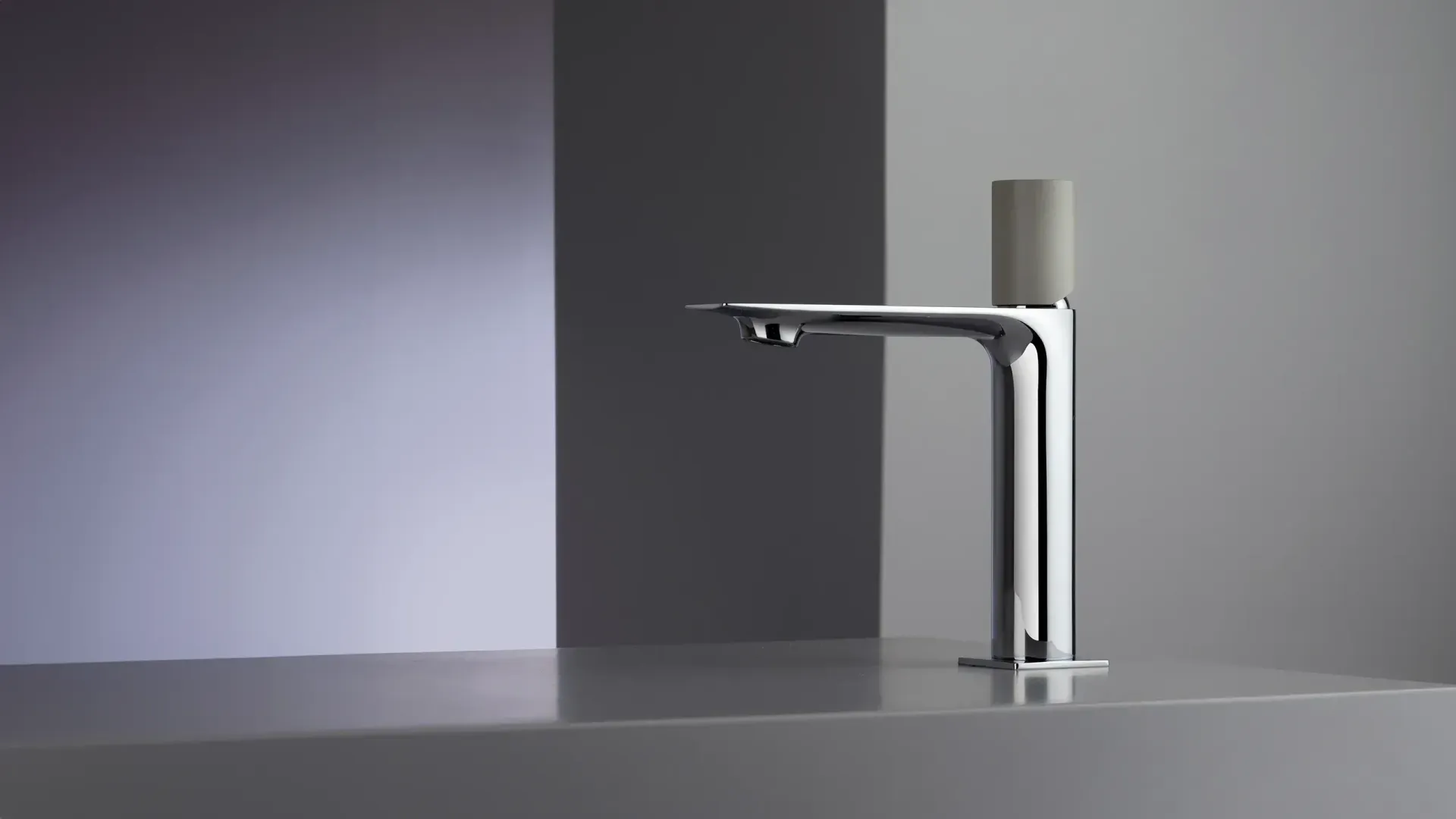 Grifo cromado con manija gris, sobre fondo gris y blanco.