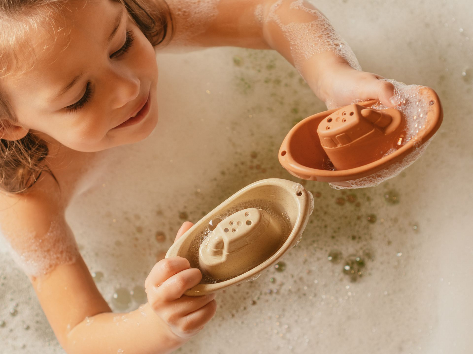 Enfant dans un bain jouant avec deux petits bateaux dans l'eau.