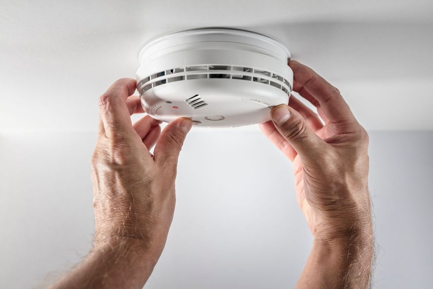 Des mains masculines installent un détecteur de fumée sur un plafond blanc.