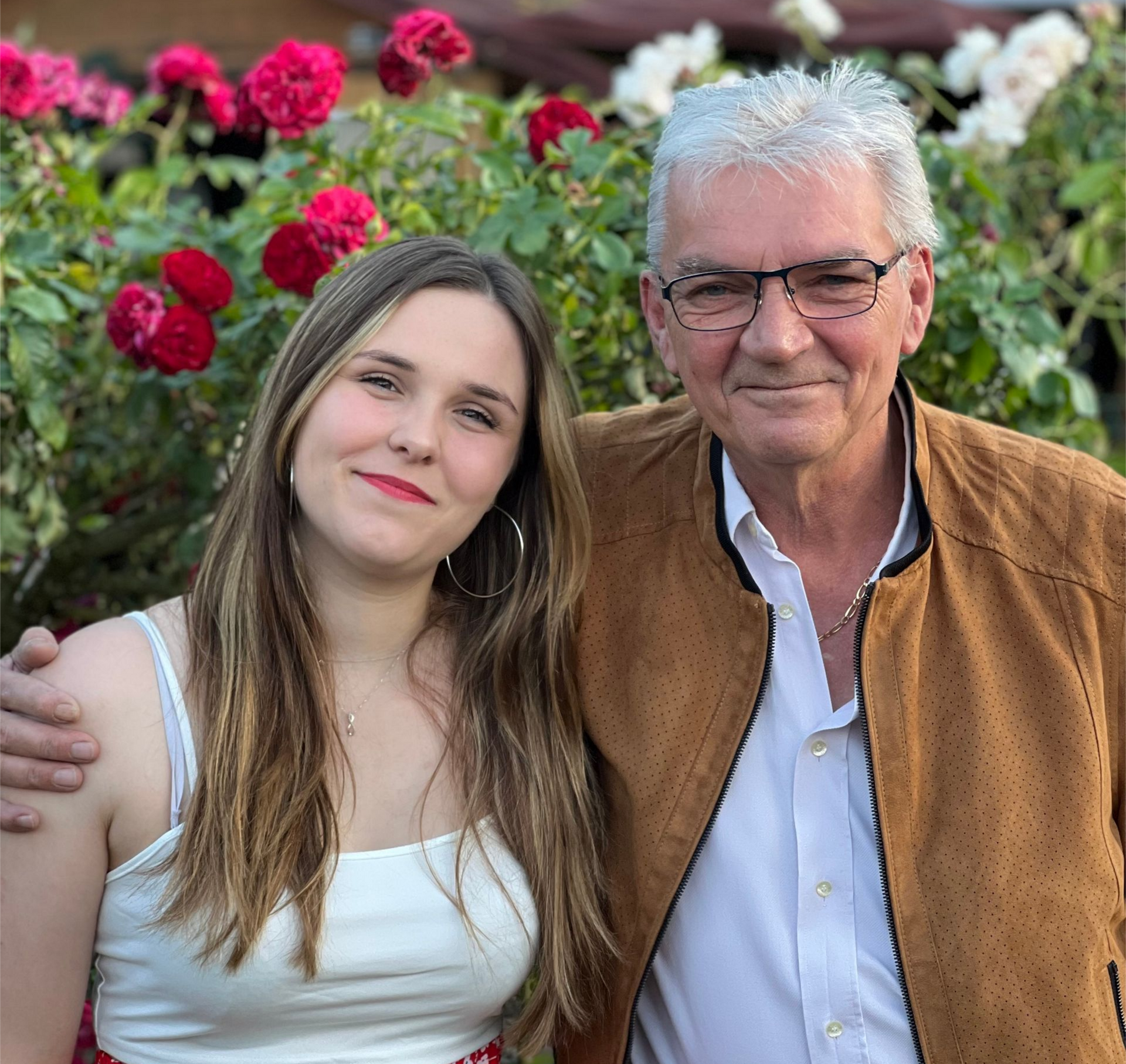 Une jeune fille et un homme posent devant des rosiers ; l'homme a le bras autour de l'épaule de la jeune fille.