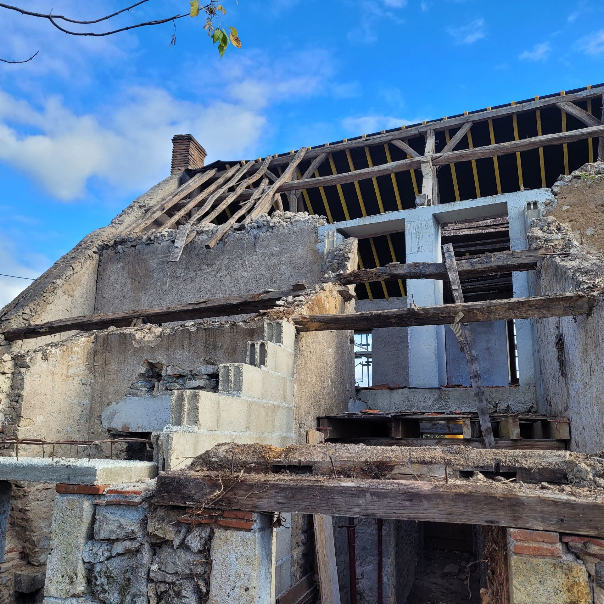 Bâtiment en pierre en ruine, toit effondré et poutres en bois apparentes sous un ciel bleu