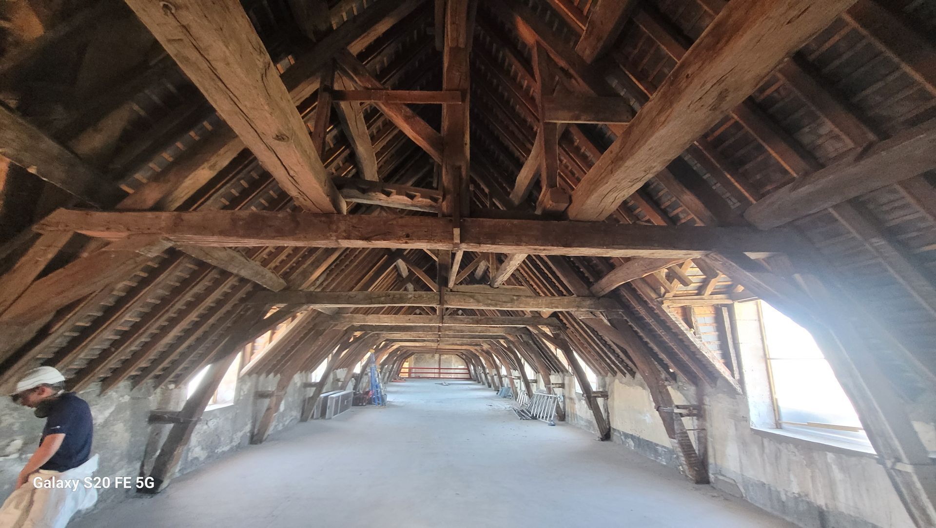 Intérieur d'un grenier rustique en bois avec poutres apparentes et une personne debout à gauche.