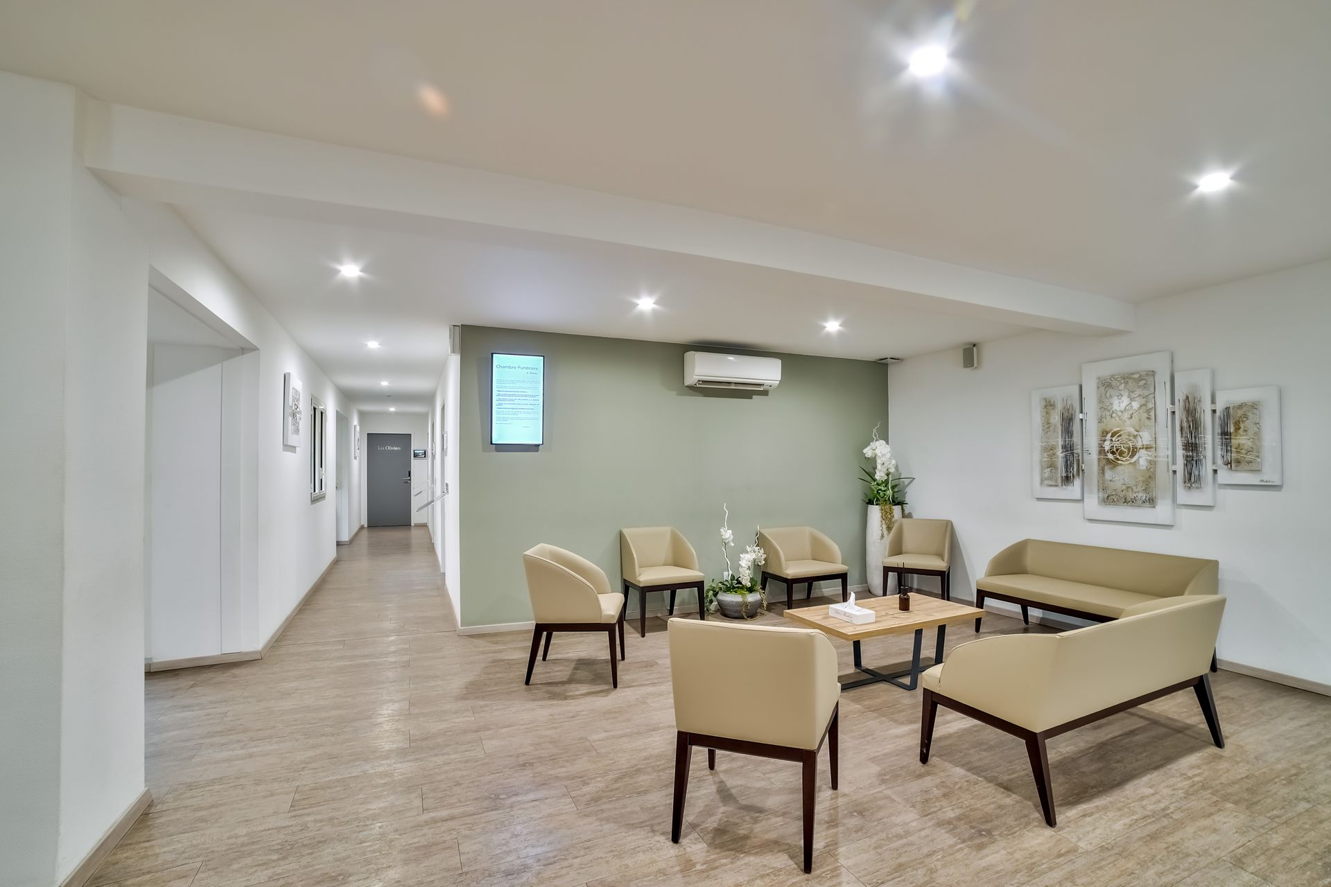 Salle d’attente moderne et spacieuse avec des fauteuils beiges, des tables basses et un couloir en arrière-plan.