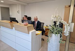 Comptoir d’accueil dans le hall d’un bureau, avec deux employés assis et une orchidée blanche au premier plan