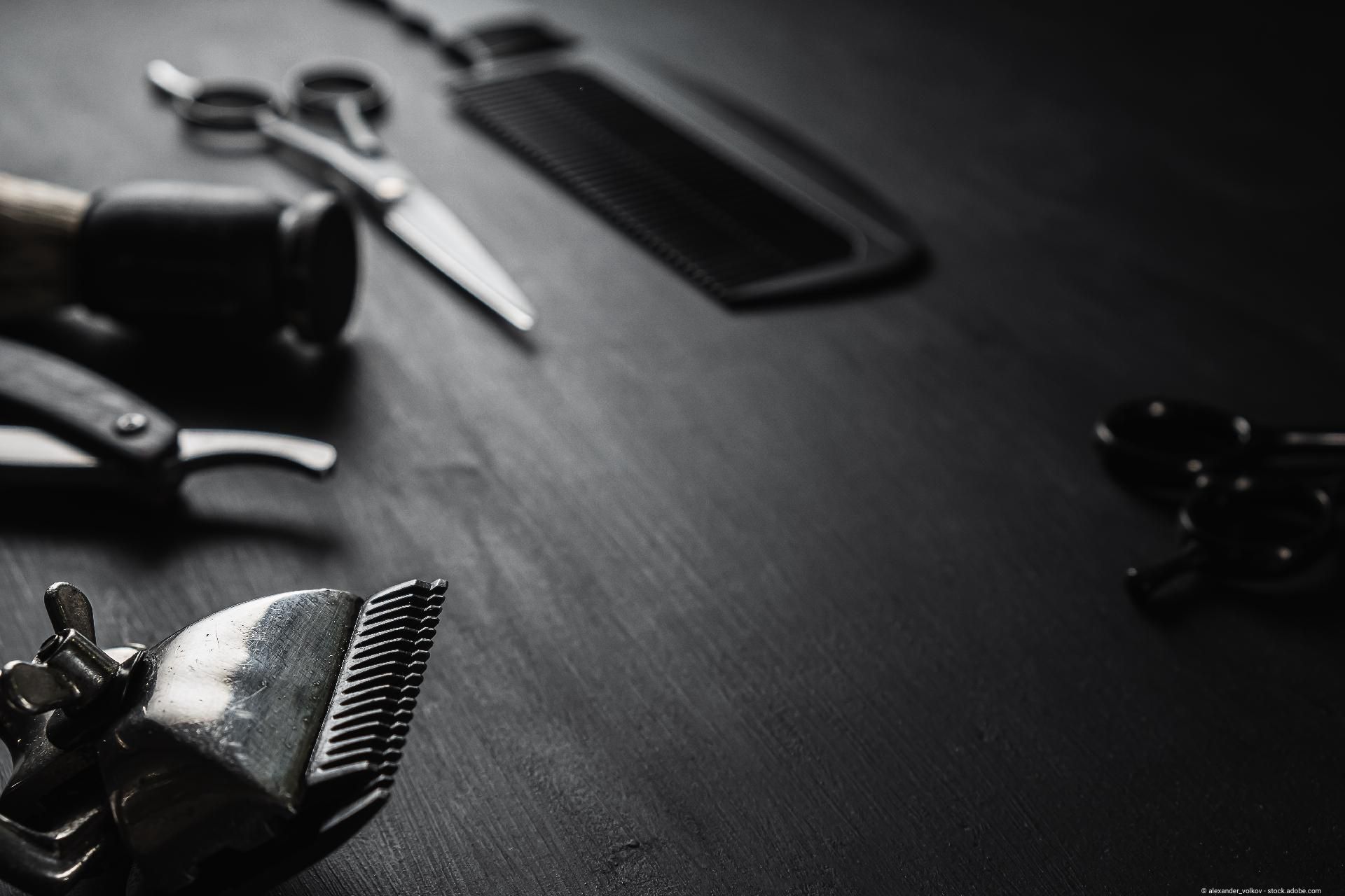 Nahaufnahme von Haarschneidemaschine, Kamm, Schere und Rasiermesser auf dunklem Untergrund.