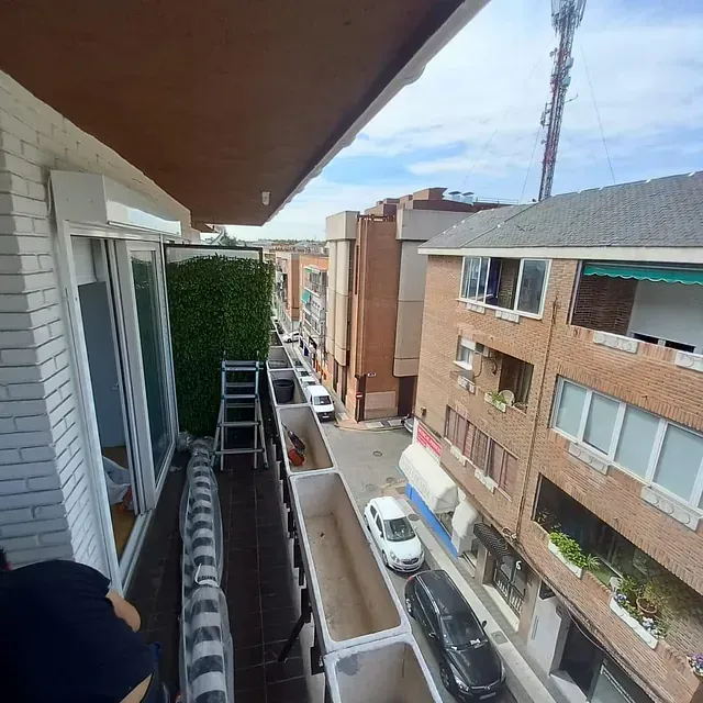 Vista desde el balcón de una calle de la ciudad con edificios, coches aparcados y un cielo despejado.